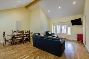 A spacious living area with a dining table, a sofa, and a television mounted on the wall. - 3 Bed in North Walsham (oc-57997) (Worstead)