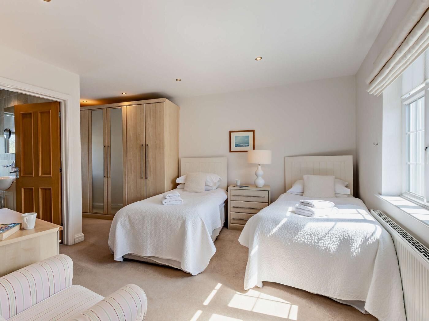 A hotel room with two beds, a wardrobe, a bedside table with a lamp, and a window.