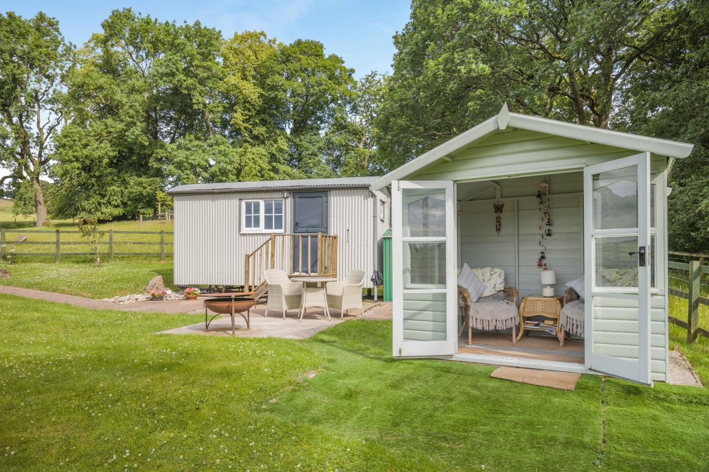 A small, single-story cottage with an open front door, a patio with outdoor furniture, and a fenced yard.