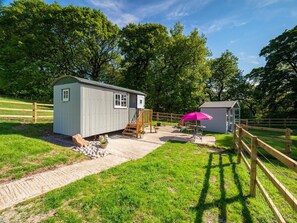 A small, single-story shed with a door and windows, a wooden deck, and a pink umbrella. - 1 Bed in Macclesfield (oc-58462) (Wincle)