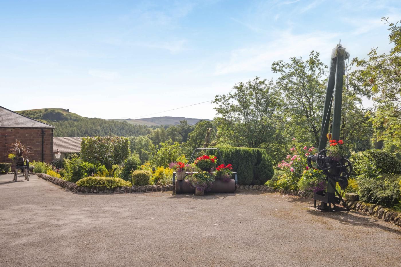 A rural property with a gravel driveway, a stone wall, and a variety of plants and flowers.