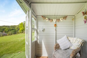 A cozy room with a wicker chair, a small table, and a view of a grassy yard. - 1 Bed in Macclesfield (oc-58462) (Wincle)