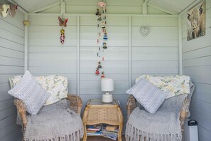 A cozy room with two wicker chairs, a small table with books, a lamp, and wall decorations including a heart-shaped ornament and a painting of a horse. - 1 Bed in Macclesfield (oc-58462) (Wincle)