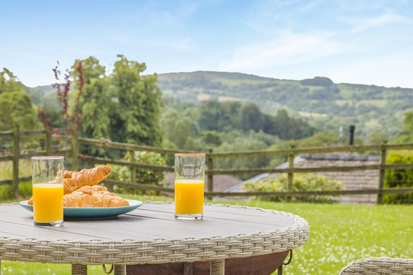 Ein Korbtisch mit Croissants und Orangensaftgläsern, vor einer malerischen Außenkulisse.