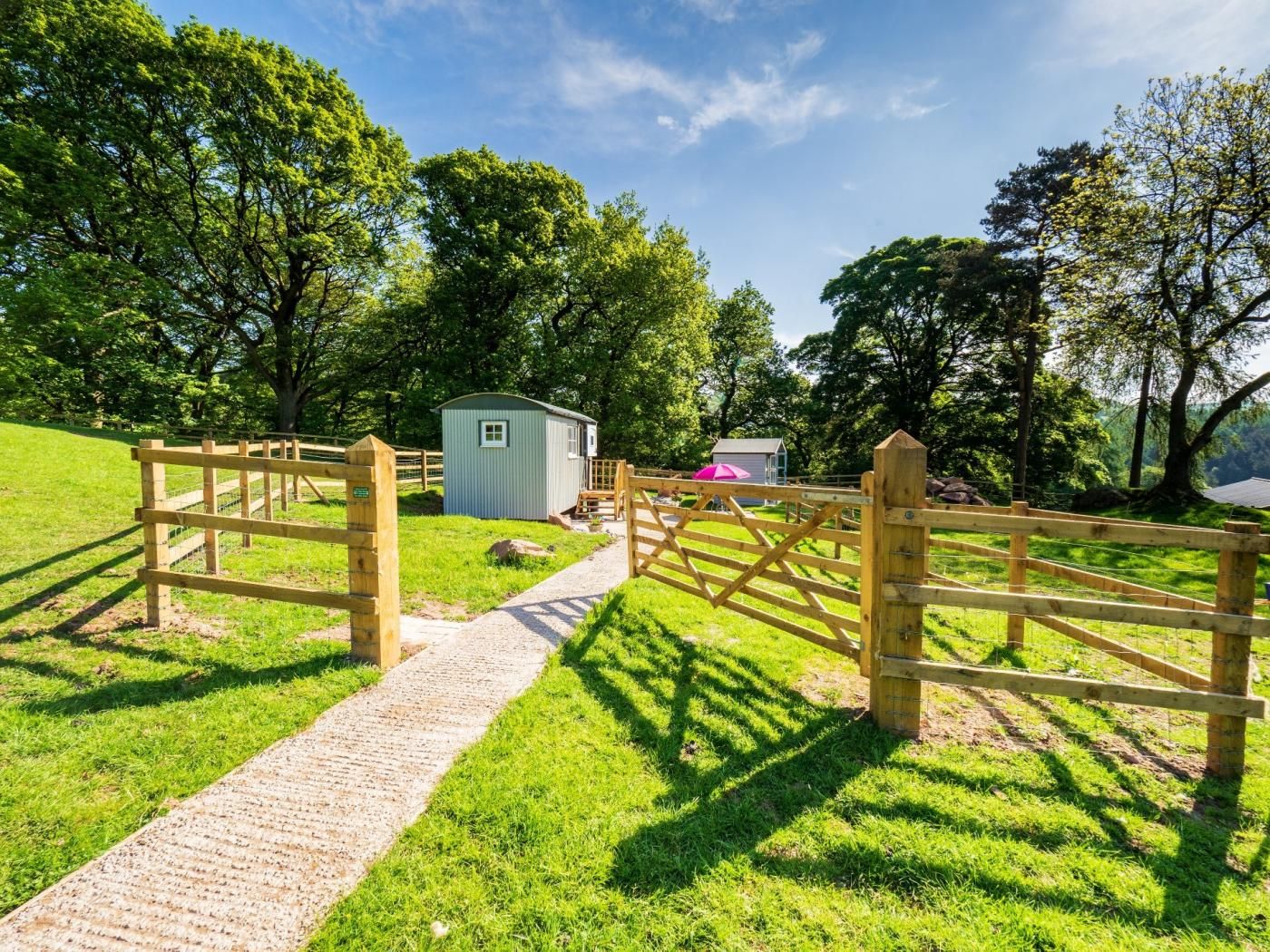 A wooden gate leading to a grassy area with a small shed and a path.