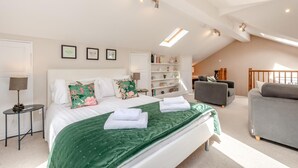 Ein Schlafzimmer mit einem großen Bett, einem grauen Sofa, einem Bücherregal und einem Oberlicht.