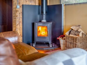 A cozy room with a wood-burning stove, a wicker basket with logs, and a leather couch. - 1 Bed in St. Austell (oc-58376) (Pentewan Valley)
