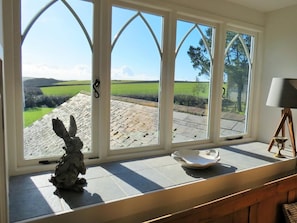 Ein Zimmer mit großem Fenster und Blick auf ein grünes Feld sowie ein Stein-Dach.