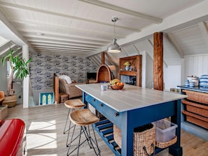 Ein geräumiges Loft mit hoher Decke, einem großen Küchentisch mit Barhocker, Kamin und Blick zum Himmel.