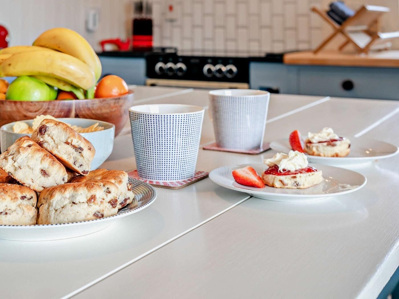 Un comptoir de cuisine avec des pâtisseries, une tasse de café et un saladier de fruits.
