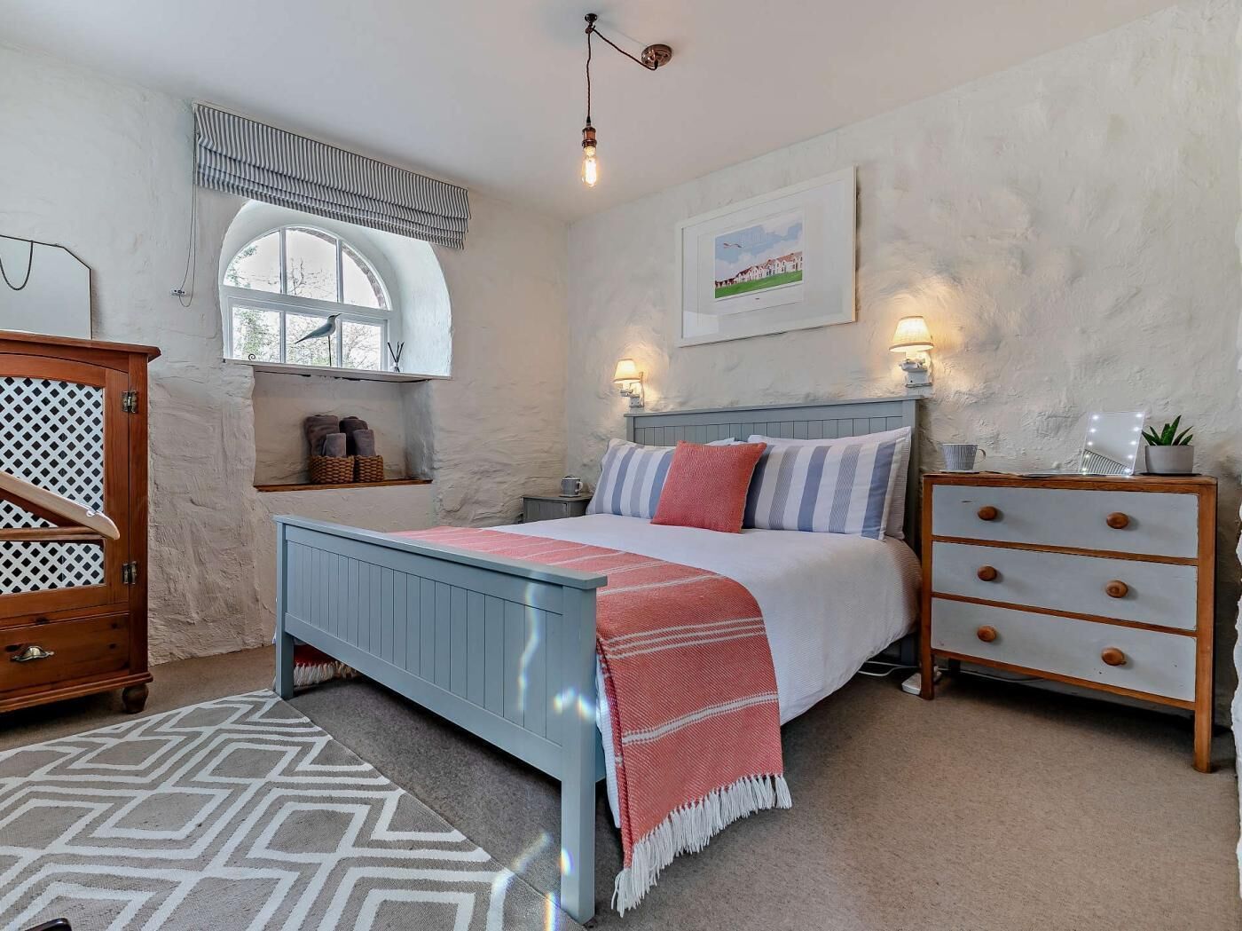 A bedroom with a bed, dresser, window, and artwork on the wall.