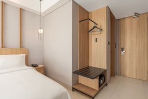 Habitación de hotel con cama, mesita de noche, lámpara colgante, perchero y armario.