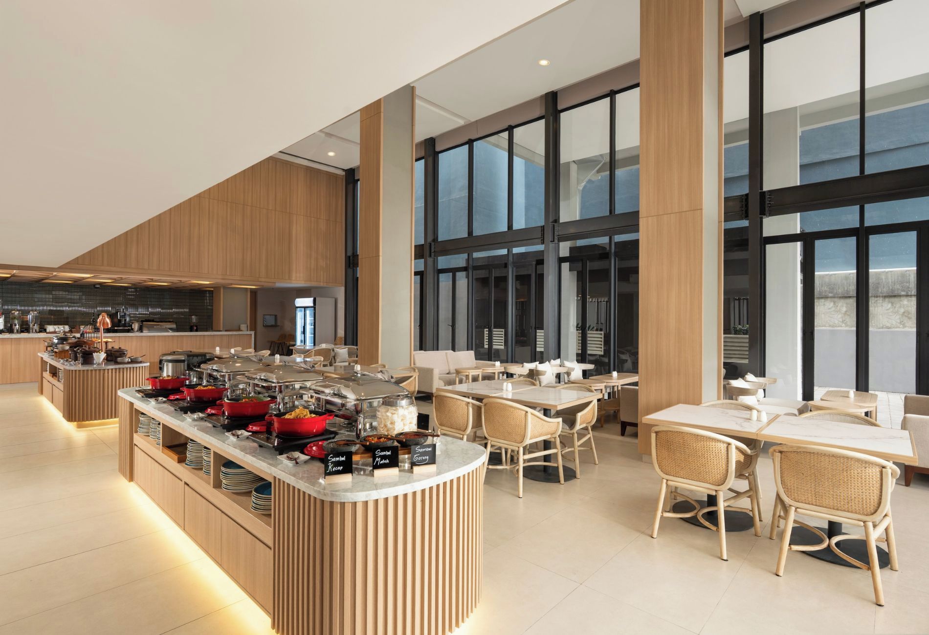 Un comedor moderno con mesas de buffet, techos altos y ventanas grandes.
