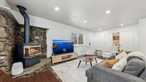 A living room with a stone wall, a fireplace, a television, and a sofa. - 2543 Knox Avenue 3 Bedroom Cabin (South Lake Tahoe)
