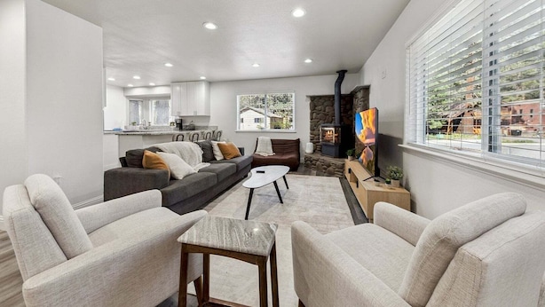 A modern living room with a sofa, chairs, a coffee table, a fireplace, and a kitchen in the background. - 2543 Knox Avenue 3 Bedroom Cabin (South Lake Tahoe)