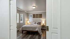 A bedroom with a bed, two bedside tables with lamps, a ceiling light, and a window with blinds. - 2543 Knox Avenue 3 Bedroom Cabin (South Lake Tahoe)
