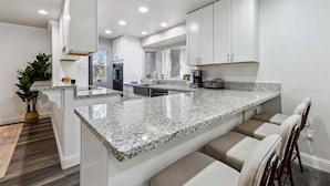 A modern kitchen with white cabinets, granite countertops, and a bar area with stools. - 2543 Knox Avenue 3 Bedroom Cabin (South Lake Tahoe)