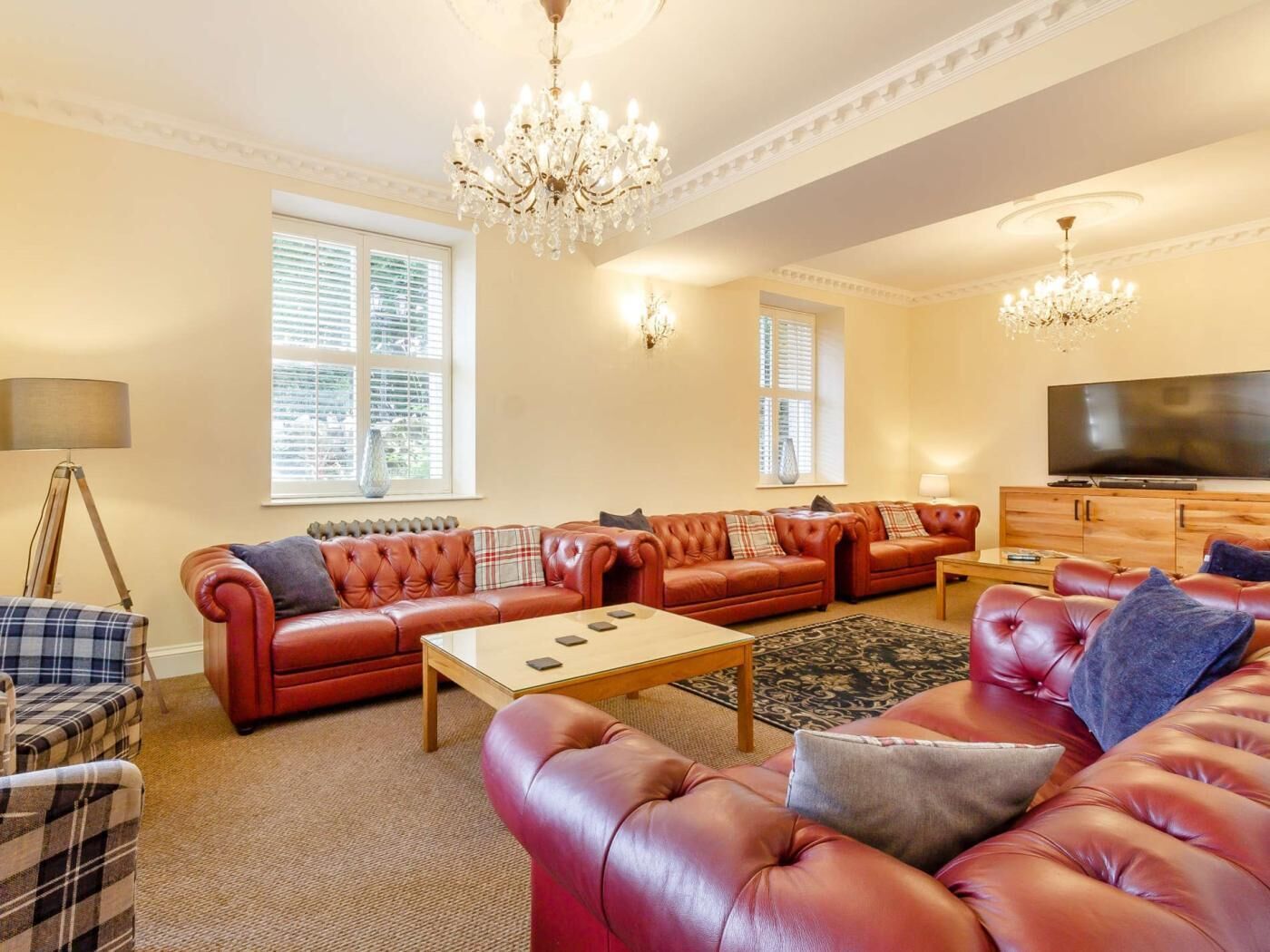 A spacious living room with leather sofas, a coffee table, a TV, and a chandelier.