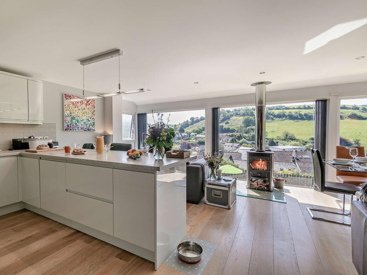 A modern kitchen with a central island, a built-in stove, and large windows offering a view of the countryside.