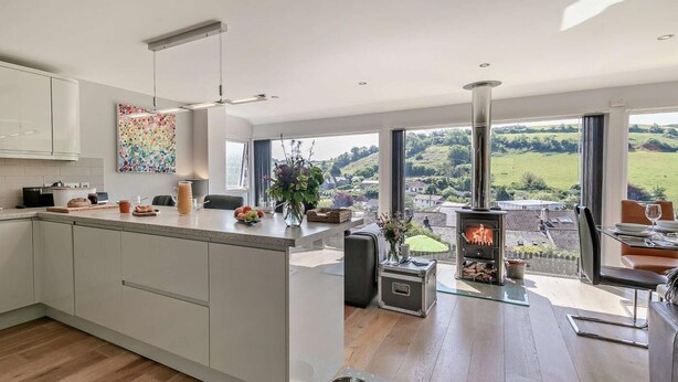 A modern kitchen with a central island, a built-in stove, and large windows offering a view of the countryside. - 4 Bed in Torpoint (oc-58602) (Millbrook)