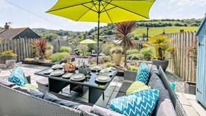 An outdoor patio with a dining table set for four, surrounded by wicker furniture and a large yellow umbrella. - 4 Bed in Torpoint (oc-58602) (Millbrook)