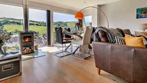 A modern living room with a fireplace, dining area, and a sofa. - 4 Bed in Torpoint (oc-58602) (Millbrook)