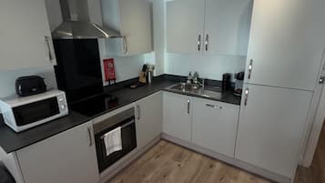Una cocina moderna con armarios blancos, una campana extractora de acero inoxidable, un microondas y un lavamanos.