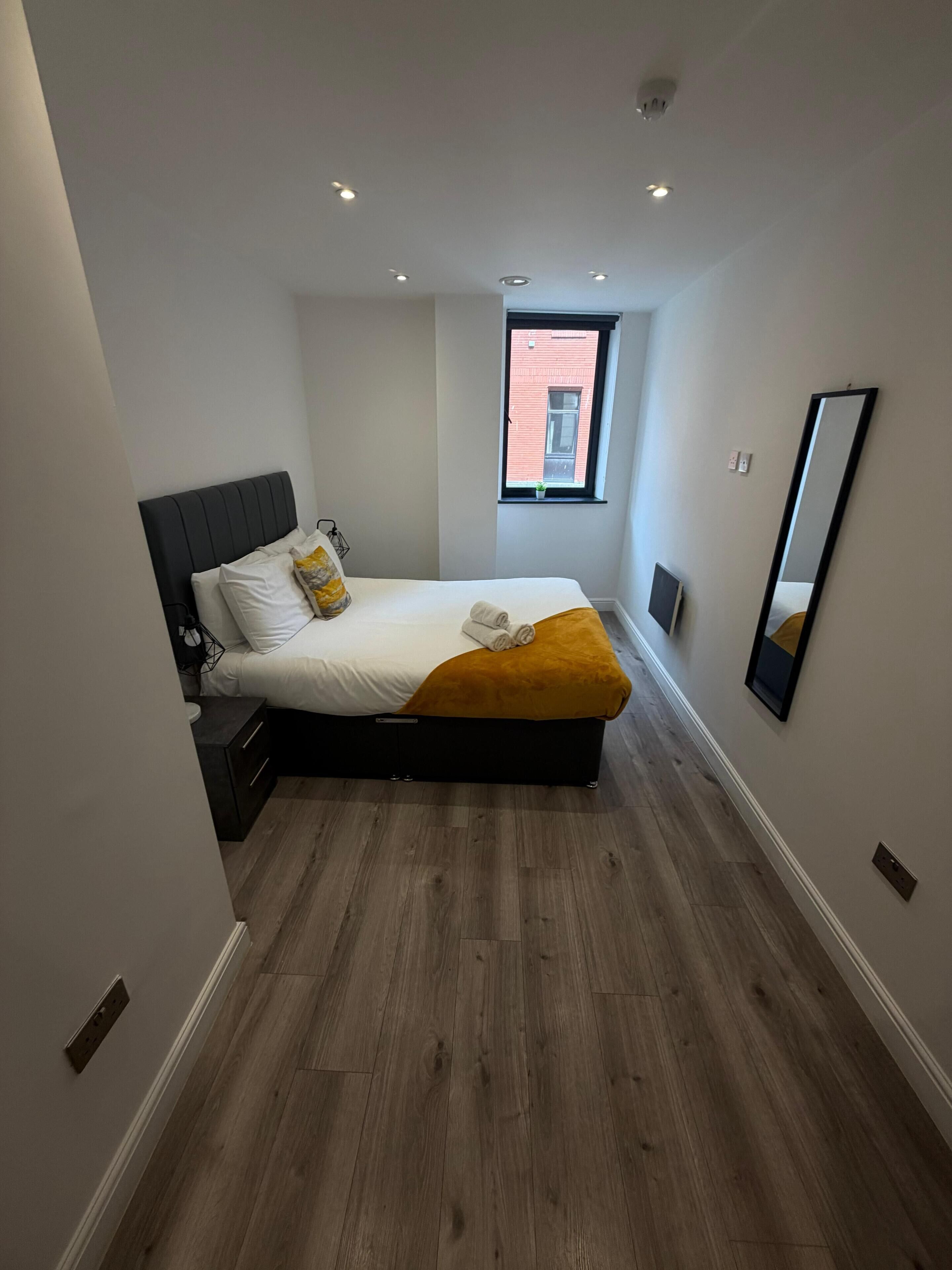 A bedroom with a bed, a nightstand, a window, and a mirror.