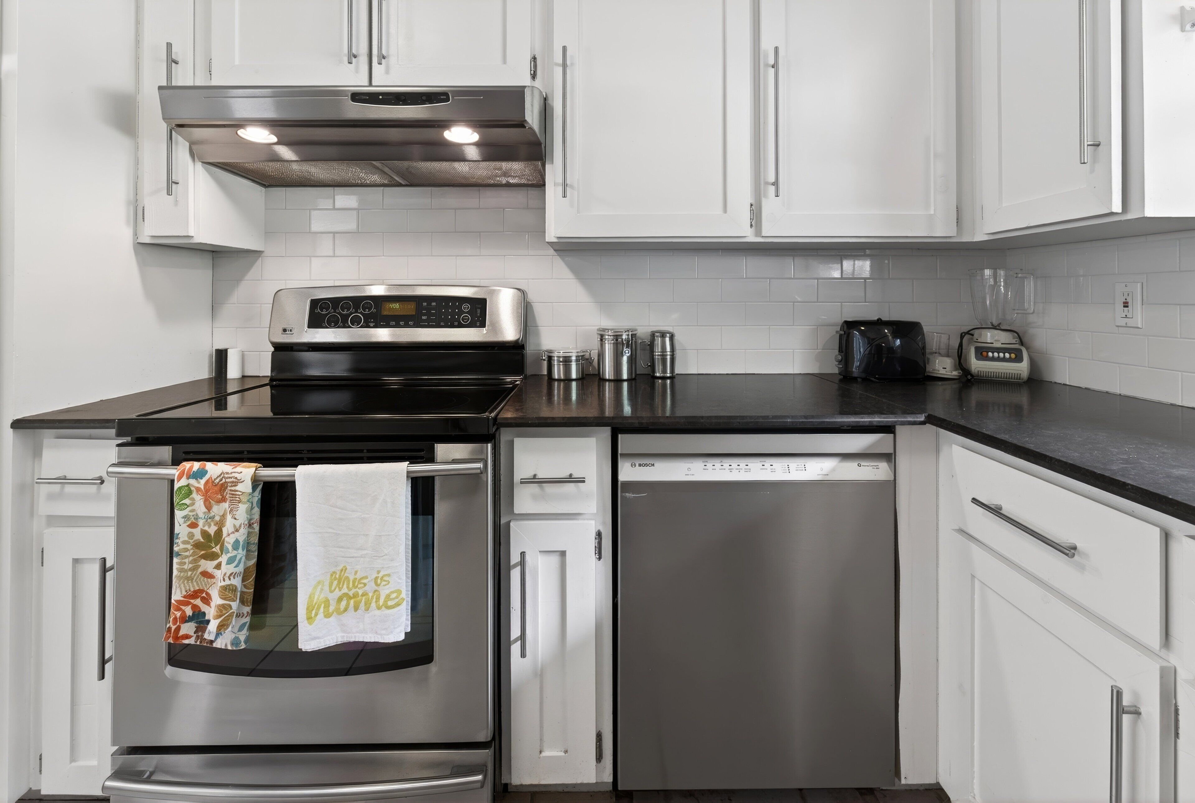 A modern kitchen with stainless steel appliances, white cabinetry, and a black countertop.