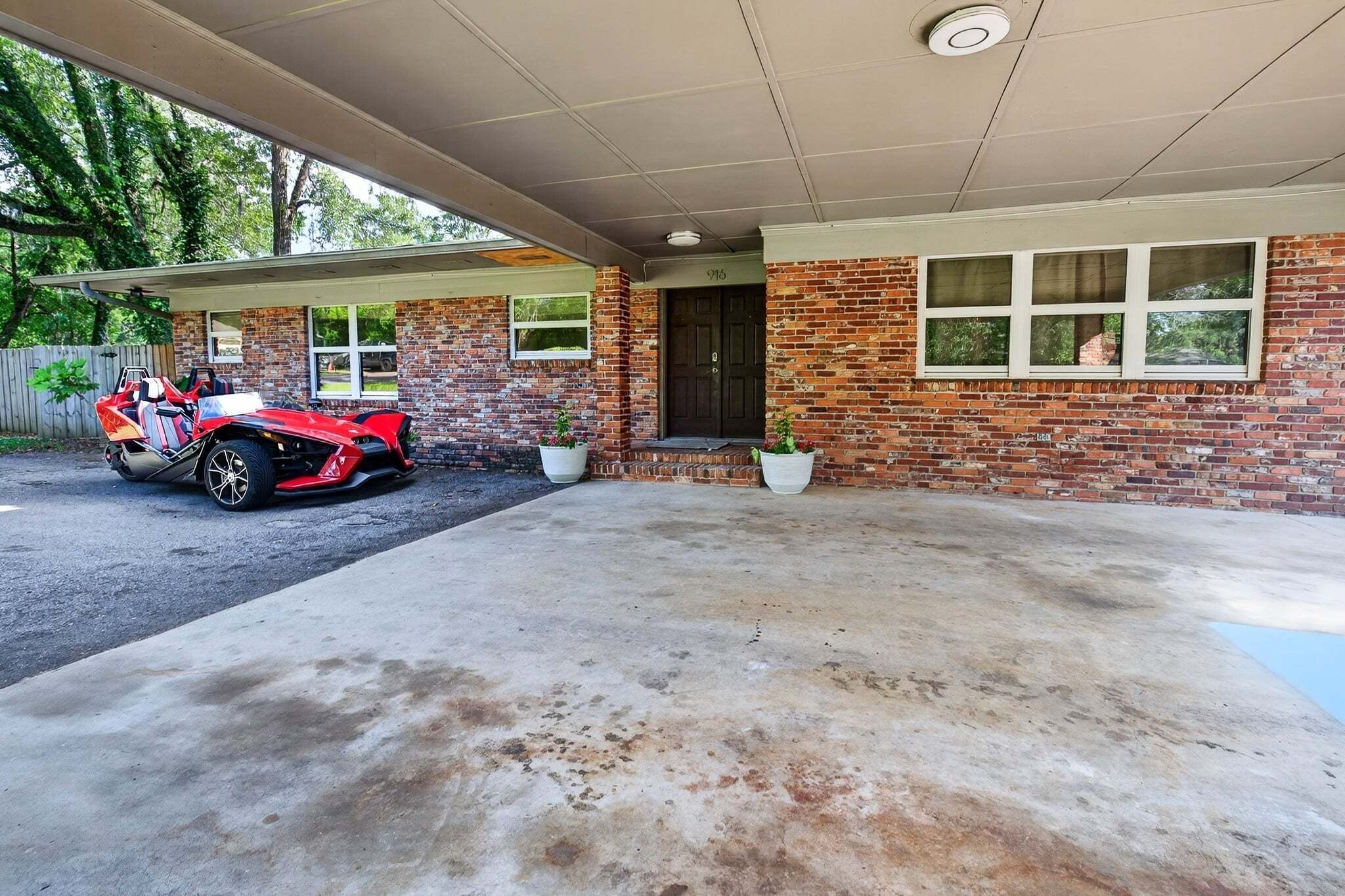 A house with a brick exterior, a covered driveway, and a red vehicle parked outside.