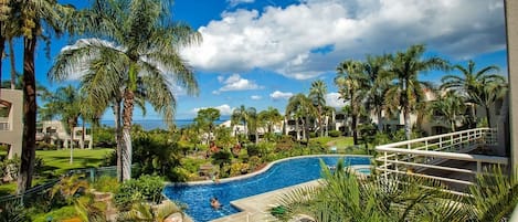 Un resort con piscina rodeada de palmeras y vista al océano.