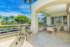 Ein Balkon mit Sitzgelegenheit im Freien, Blick auf Palmen und ein Gebäude im Hintergrund.