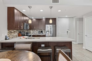 A modern kitchen with dark wood cabinets, stainless steel appliances, and a large island with bar stools. - Villa Grand 2 Bedroom Condo (Phoenix)