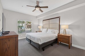 Ein Schlafzimmer mit einem Bett, Nachttischen, einem Deckenventilator und einem Fenster mit Jalousien.