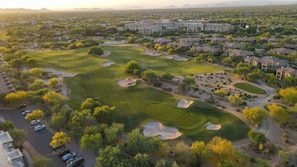An aerial view of a golf course with sand bunkers, a parking area, and residential buildings in the background. - Villa Grand 2 Bedroom Condo (Phoenix)