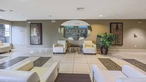 A lobby with a reception desk, two armchairs, a potted plant, and a large wall-mounted sign. - Villa Grand 2 Bedroom Condo (Phoenix)