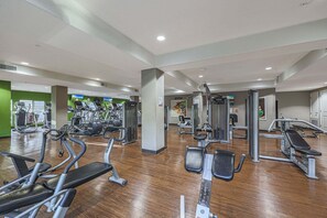 Ein Fitnessstudio mit verschiedenen Trainingsgeräten, einer zentralen Säule und einer grünen Wand.