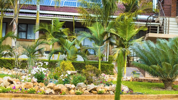 A house with solar panels, a brick exterior, and a well-maintained garden with various plants and rocks.
