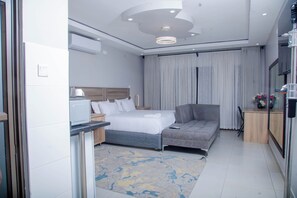 A modern hotel room with a bed, a sofa, a desk with a computer, and a television.