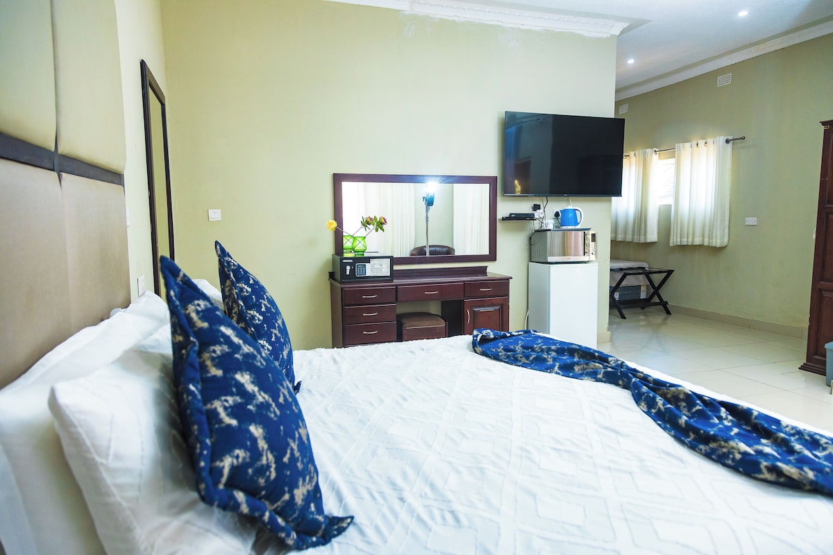 A hotel room with a bed, a desk, a mirror, a television, and a window with curtains.