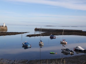 A calm harbor with several boats anchored, a lighthouse in the background, and a breakwater extending into the water. - 3 Bed in Seahouses (oc-cn003) (Seahouses)
