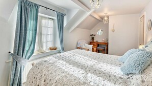 A bedroom with a sloped ceiling, a bed with a white lace cover, a wooden desk, a chair, a hanging light fixture, and a window with blue curtains. - 3 Bed in Backworth (oc-cn013) (Backworth)