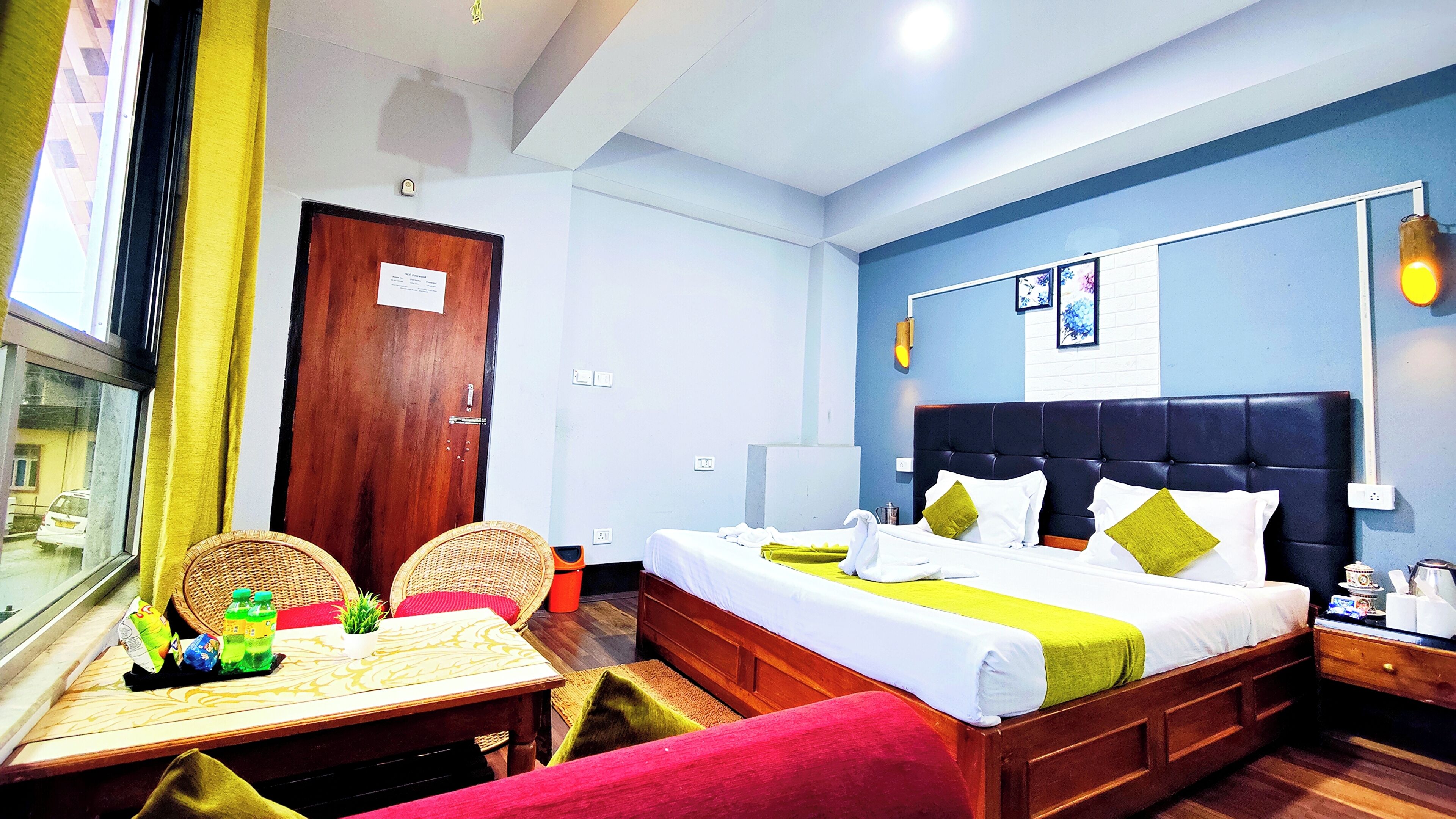 A hotel room with a bed, bedside table, chairs, a window, and a door.
