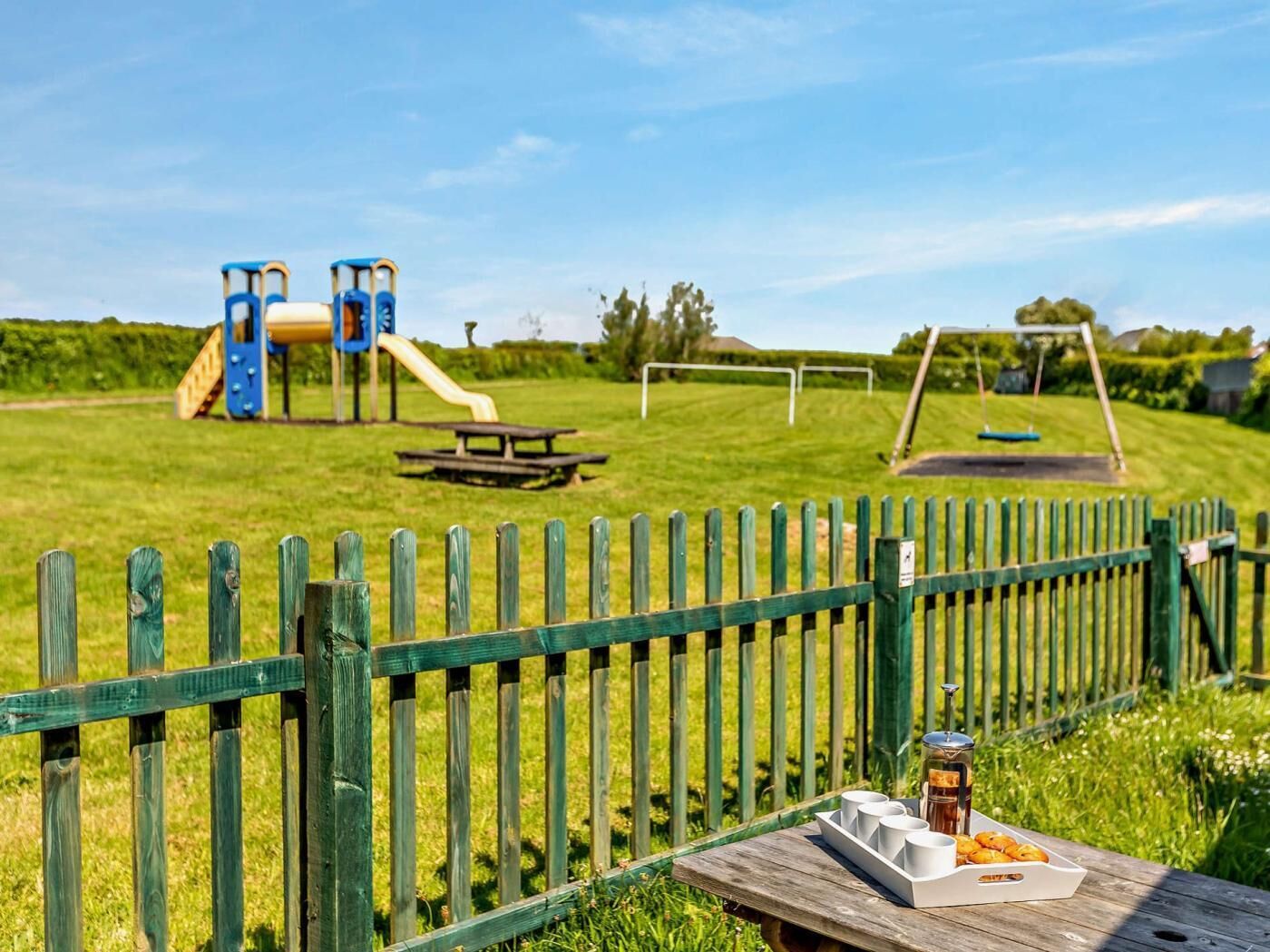 Une aire de jeux avec des toboggans et des balançoires, une table de pique-nique et une clôture en bois.