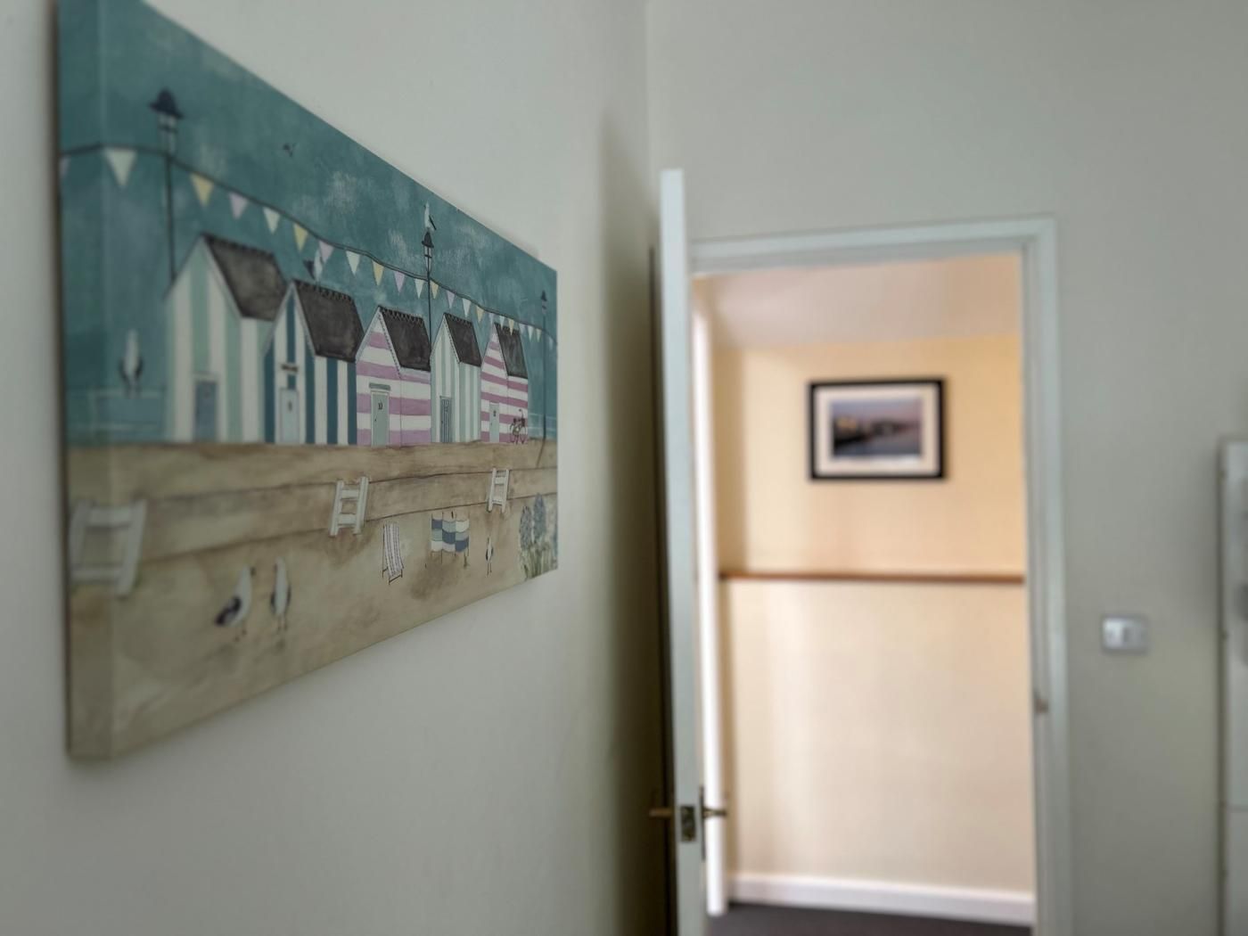 Un corridoio con un quadro raffigurante case sulla spiaggia a righe e una porta che dà su una stanza con un quadro incorniciato.