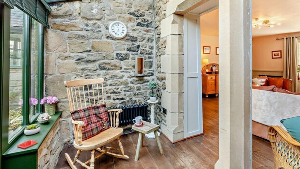 A stone-walled room with a wooden rocking chair, a small table, and a clock on the wall. - 3 Bed in Backworth (oc-cn011) (Backworth)