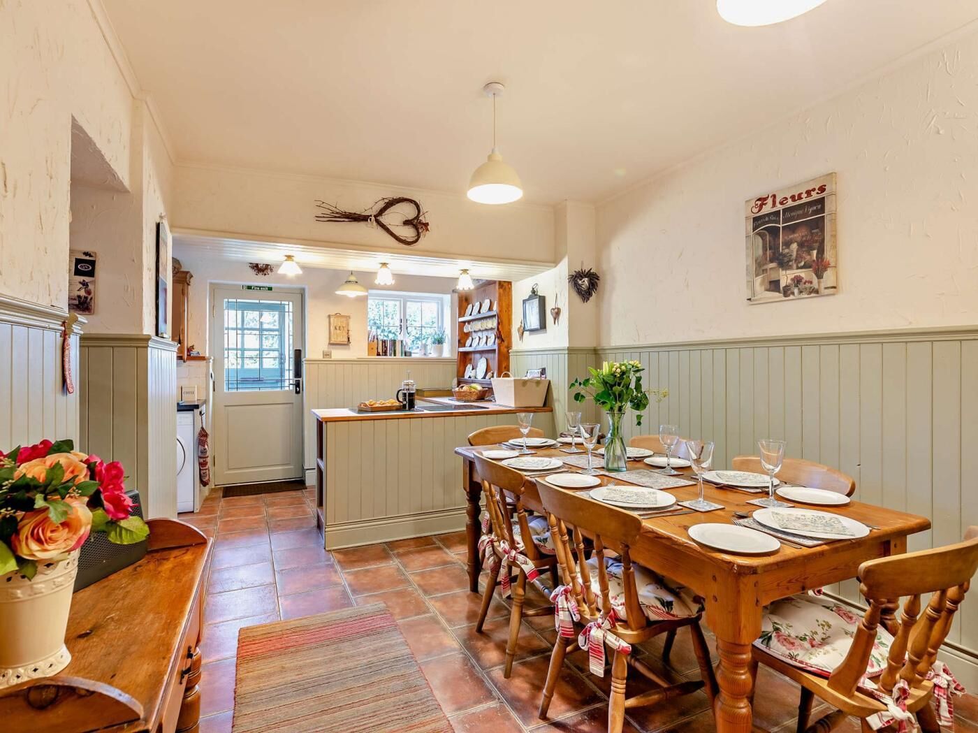 A dining area with a wooden table set for four, surrounded by wooden chairs with red and white checkered seat covers.