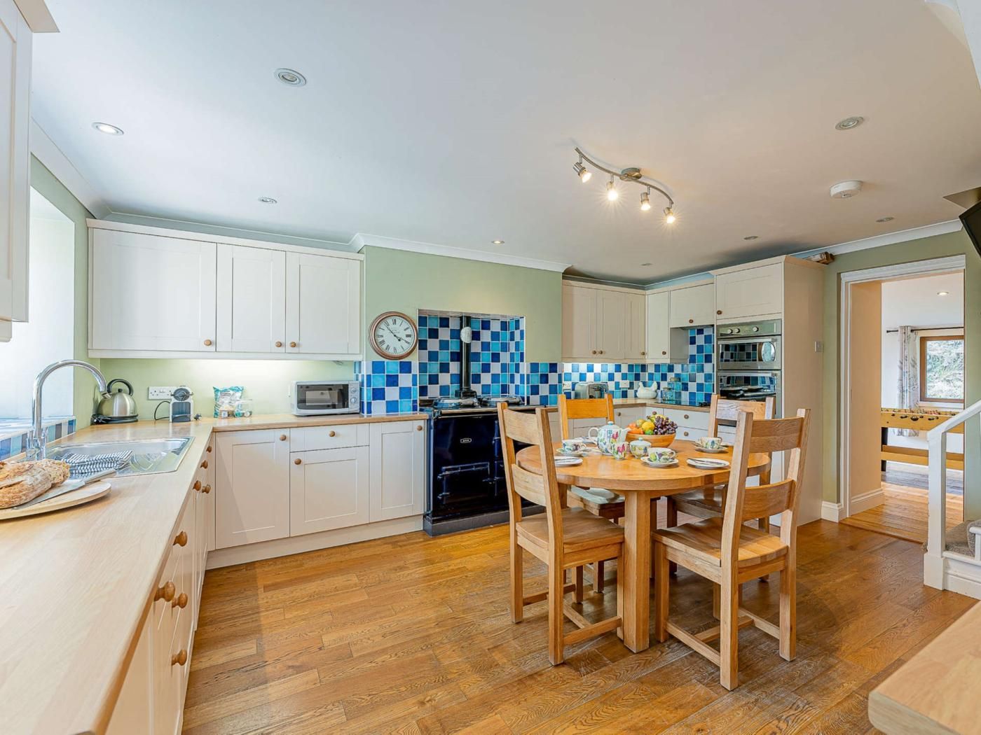 Cozinha moderna com armários brancos, painel de backsplash xadrez azul e branco, e área de jantar com cadeiras de madeira.