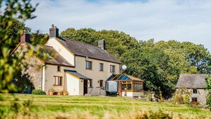 A two-story house with a conservatory, a stone chimney, and a well-maintained lawn. - 5 Bed in Aberystwyth (oc-58889) (Llanrhystyd)