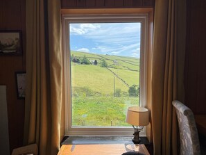 Ein Zimmer mit großem Fenster und Blick auf ein grünes Feld sowie einen entfernten Hügel.
